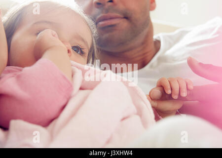 Baby girl sucking thumb with comfort blanket on father's lap Stock Photo