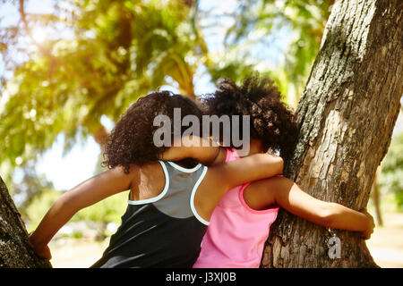 Two young sisters playing on tree. rear view Stock Photo