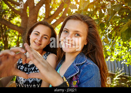 Portrait of two female friends in rural setting, making heart shape with hands Stock Photo