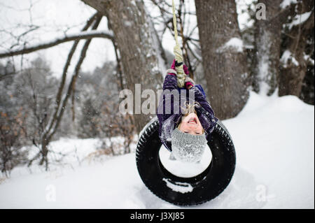 Girl upside down on tire swing in snow Stock Photo