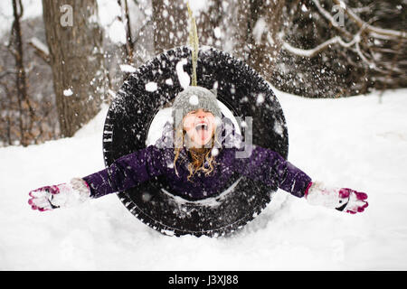 Girl playing in snow on tire swing Stock Photo