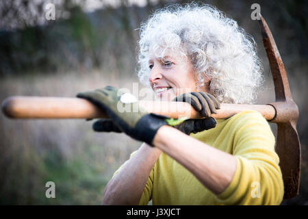 Mature woman carrying pick axe over her shoulder in landscape Stock