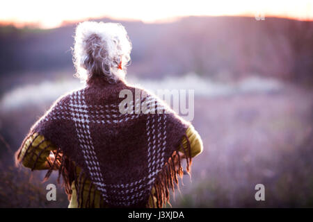 Rear view of mature woman watching sunset over rural landscape Stock Photo