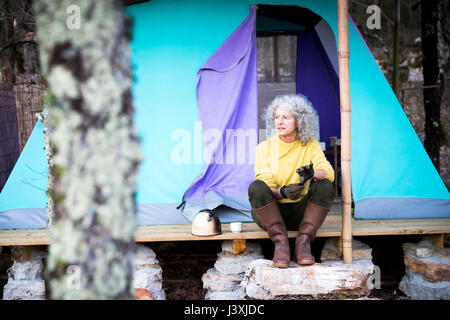 Mature woman sitting on woodland camping porch Stock Photo