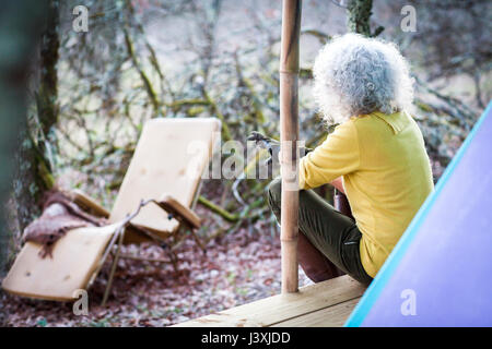 Mature woman looking out from woodland camping porch Stock Photo