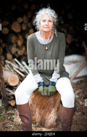 Portrait of mature grey haired woman sitting on log in garden Stock Photo