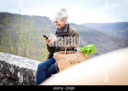 Woman sitting on wall texting on smartphone, Bruniquel, France Stock Photo