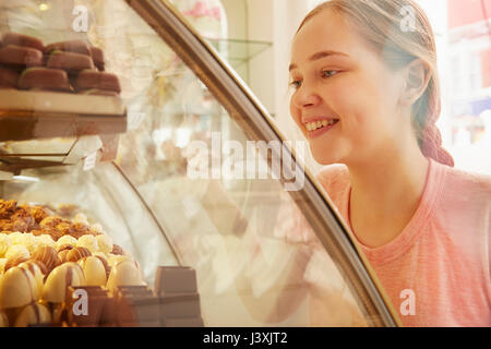 Girl in bakery looking at cakes in display cabinet smiling Stock Photo