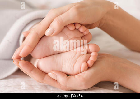 Mother cupping baby's feet on bed Stock Photo