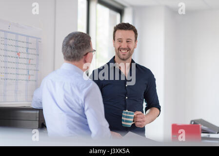 Male colleagues talking by photocopier machine Stock Photo