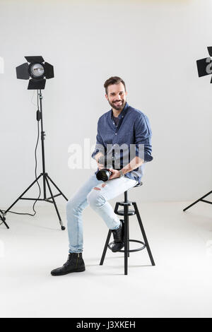 Portrait of male photographer sitting on white background in photographers studio Stock Photo