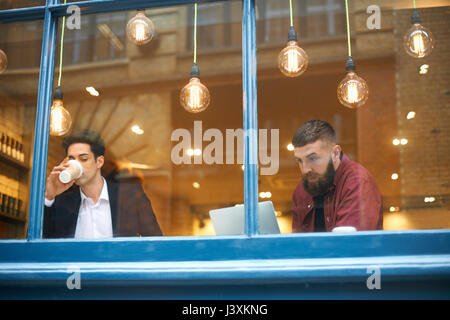 Window view of businessmen drinking coffee and using laptop in cafe Stock Photo