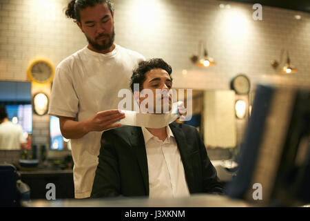 Barber preparing businessman for shave in barber shop Stock Photo