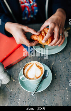 Overhead view of woman's hand holding croissant in cafe Stock Photo