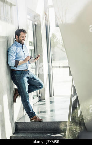 Businessman leaning against office wall using digital tablet touchscreen Stock Photo