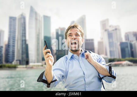 Ecstatic businessman holding smartphone on city waterfront Stock Photo