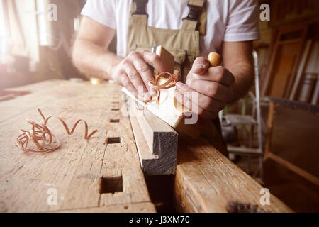 Mid section of male carpenter using wood plane at workbench Stock Photo