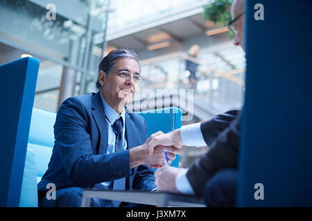 Two businessmen shaking hands in office atrium Stock Photo