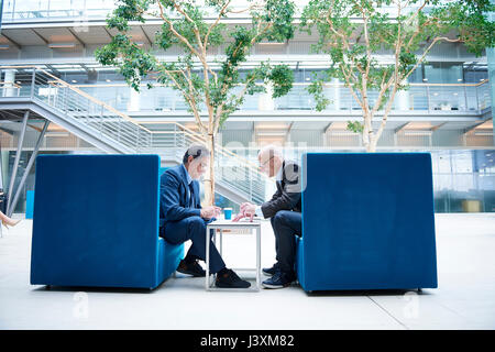 Two businessmen having discussion meeting in office atrium armchairs Stock Photo