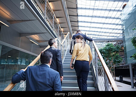 Rear view of businesswoman and men moving up office stairway Stock Photo