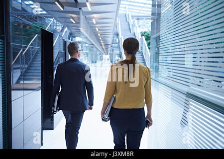 Rear view of businesswoman and man walking through office atrium Stock Photo
