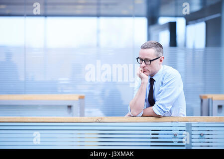 Stressed businessman with chin on hand in office atrium Stock Photo