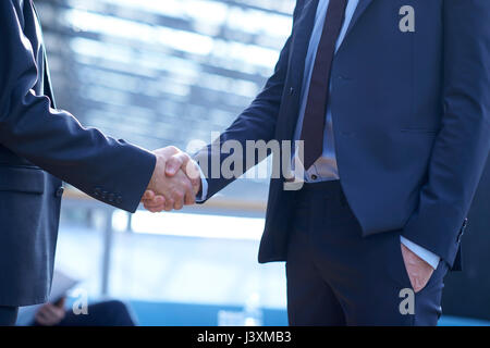 Mid section of two businessmen shaking hands in office atrium Stock Photo