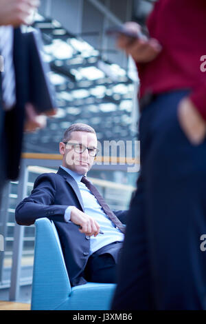 Businessman sitting on sofa in office atrium Stock Photo