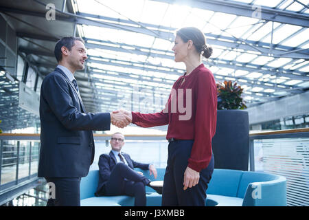 Businessman and woman shaking hands in office atrium Stock Photo