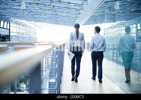 Rear view of businessman and woman walking on office balcony Stock Photo