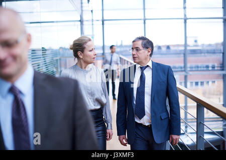 Businessmen and woman walking and talking on office balcony Stock Photo