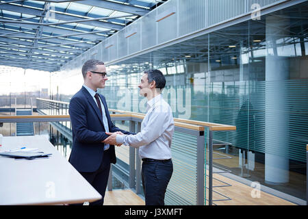 Two businessmen shaking hands on office balcony Stock Photo