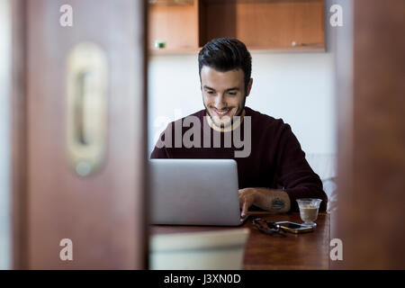 Young man sitting at table using laptop Stock Photo