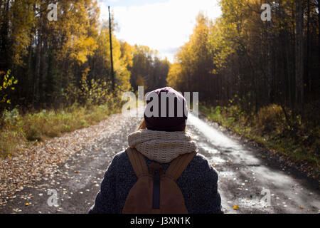 Young woman hiking, on empty country road, rear view, Sverdlovsk Oblast, Russia Stock Photo