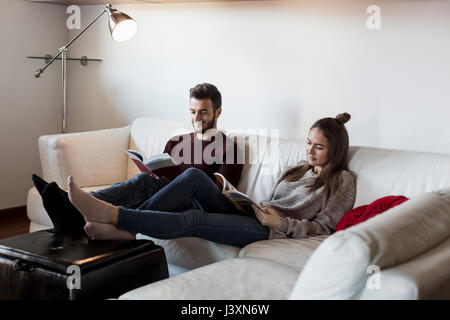 Young couple, relaxing on sofa, reading magazines Stock Photo