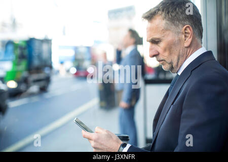 Businessman waiting at bus stop using smartphone, London, UK