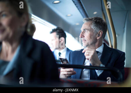 Businessman listening to smartphone earphones on double decker bus Stock Photo