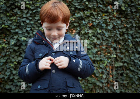 Portrait of red haired boy in front of ivy wall fidgeting with hands Stock Photo