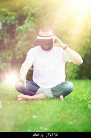 Young bearded man wearing virtual reality goggles sitting in his garden. Lifestyle VR fun and relax concept. Stock Photo