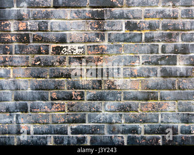 Section of red brick wall with distressed black painted bricks with peeling paint Stock Photo