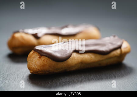 two eclairs with dark chocolate on top on slate background Stock Photo