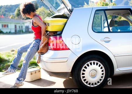 Woman struggling to push luggage into car boot Stock Photo