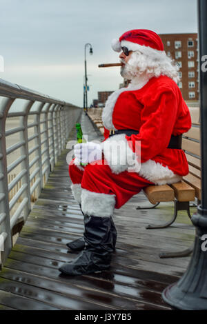 Man dressed in Santa suit, sitting on bench, smoking cigar, holding bottle of beer Stock Photo