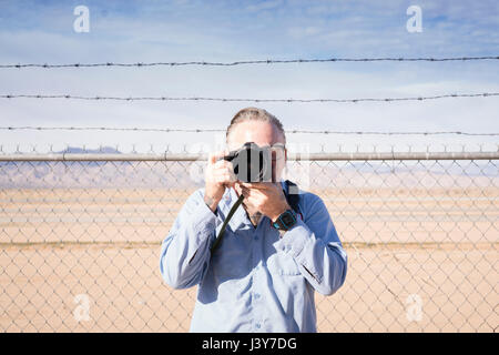 Photographer in front of barbed wire fence in desert taking photograph, California, USA Stock Photo