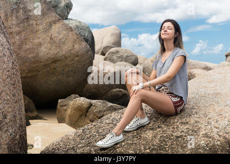 Teenage girl sitting on rocks, eyes closed, relaxing Stock Photo