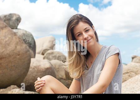 Portrait of teenage girl sitting on rocks looking at camera smiling Stock Photo