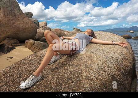 Teenage girl lying on rock sunbathing Stock Photo