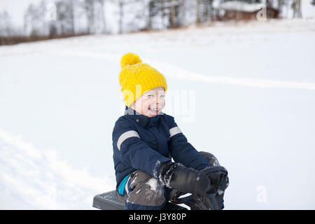 Young boy sitting on sledge, in snow covered landscape Stock Photo