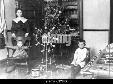 A woman and [probably] her sons, with a small table Christmas tree, c.1916.  They pose in the kitchen of an above-average home. I think the woman is a servant in the house, and this is her family's Christmas celebration.  To see my other Christmas-related vintage images, Search:  Prestor  vintage  holiday Stock Photo