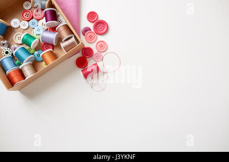 box with thread spools and sewing buttons on table Stock Photo